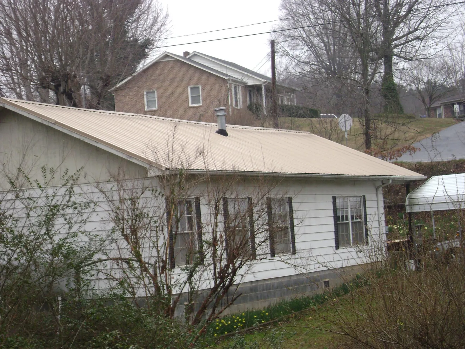 Tan metal roof on a white sided house set into a hillside — Commercial Roofing by Roofing Brothers in Howell